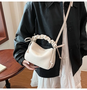 Close-up of cream-colored shoulder bag featuring a pleated handle and drawstring knot detail