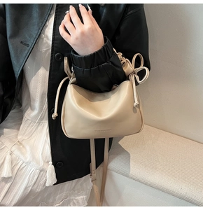 Detail view of the drawstring closure and bow decoration on a cream shoulder bag
