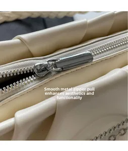 Detailed macro view of the glossy silver metal zipper head on a beige pleated handbag
