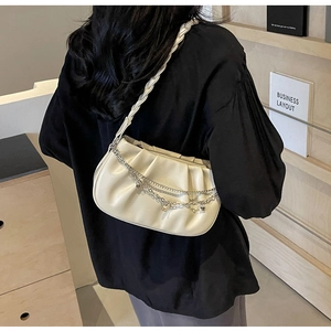 Detail of a creamy pleated shoulder bag with silver heart charms and woven strap