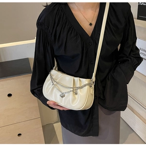 Détail du sac bandoulière plissé crème avec chaînes argentées et pendentif en cœur