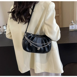 Détail du sac plissé noir avec chaînes argentées et breloque cœur sur une veste jaune