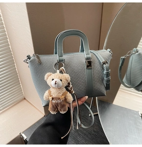 Detail of light blue textured bucket bag with a cute brown teddy bear plush charm