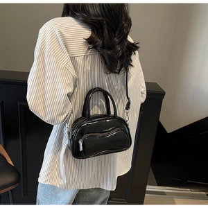 Detail view of a black glossy crossbody bowling bag shown on a model with stripe shirt