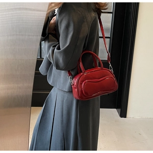 Détail d'un sac Boston en cuir verni rouge foncé porté avec un tailleur gris