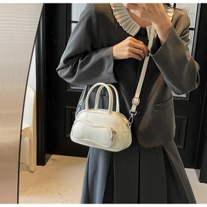 Détail d'un sac Boston blanc avec poche zippée ondulée et finitions métalliques argentées