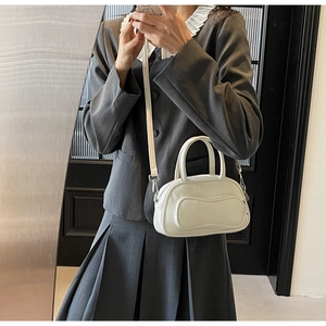 Model wearing a cream bowling crossbody bag with a round silhouette and fine texture