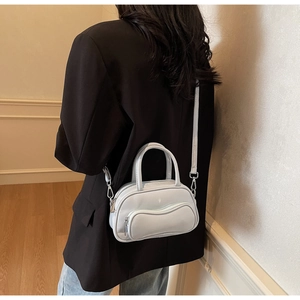 Petit sac Boston gris minimaliste porté en bandoulière dans un décor intérieur