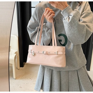 Pink patent leather shoulder bag with heart charm shown in a lifestyle model shot