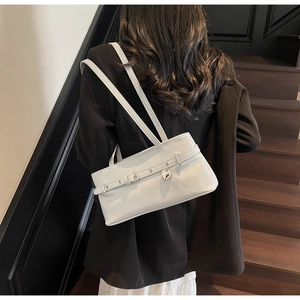 Détail du sac sous le bras blanc brillant avec pendentif cœur sur l'épaule du modèle