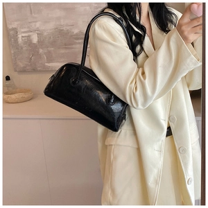Detail of minimalist black leather baguette bag with subtle wrinkled texture and brand stamp
