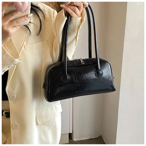 Detail showing the glossy leather texture and embossed logo on the black baguette bag