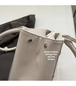 Dettaglio del bottone a pressione in metallo e cuciture rinforzate sulla borsa beige