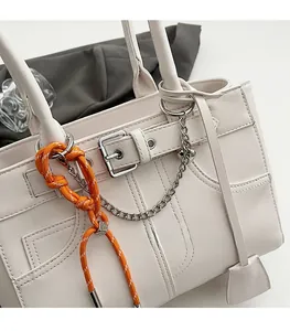 Dettaglio della borsa tote in pelle bianco sporco con nodo arancione e catena in metallo