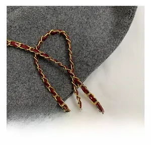 Detail of woven gold metal chain strap with deep red leather on a gray wool background