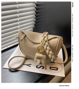 Detail of beige lychee leather bag featuring a woven strap and elephant charm