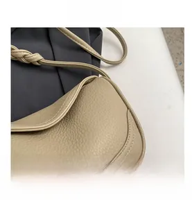 Detail view of beige pebbled leather texture and woven shoulder strap on a crossbody bag