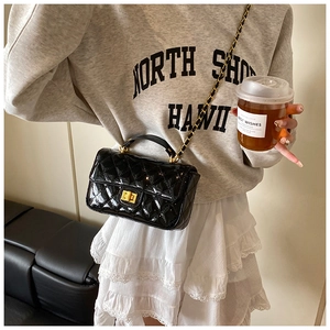 Detail of black quilted patent leather chain bag with golden clasp and top handle