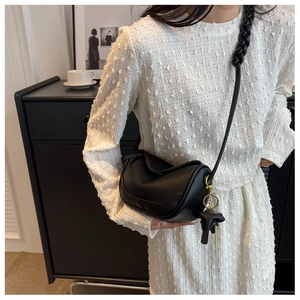 Detail of black textured leather dumpling bag featuring a woven strap and horse charm