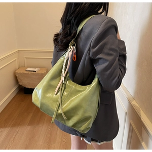 Détail du sac hobo en cuir vert avec un charm en corde tressée colorée sur la bandoulière