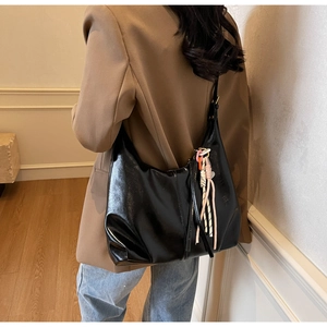 Détail du sac hobo noir brillant avec pendentif en corde tissée colorée sur la bandoulière