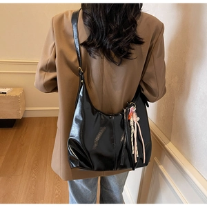 Détail du sac à bandoulière noir brillant avec breloque tissée et large sangle réglable