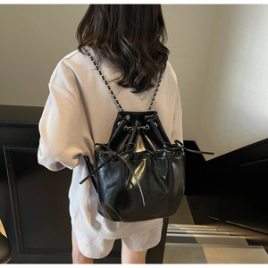 Detail of a black shiny drawstring bucket backpack with a bow and chain straps