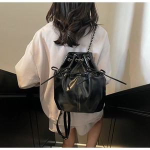 Detail view of black drawstring backpack with bow accents and chain straps on model