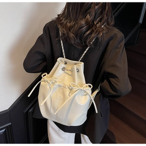 Cream bucket backpack with bow detail and chain straps worn on a black blazer