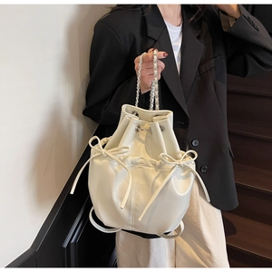 Close-up of cream-colored drawstring bucket bag featuring bow ties and chain strap