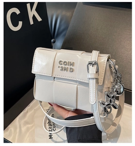 Détail du sac bandoulière tressé crème avec breloque chien ballon et logo de marque