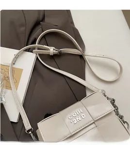 Gros plan du sac carré crème avec logo argenté et bandoulière sur une veste de costume