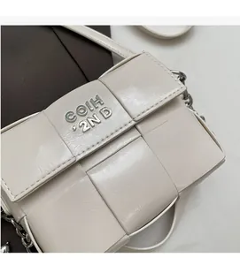 Détail de la texture tressée du sac à bandoulière crème avec logo en métal argent
