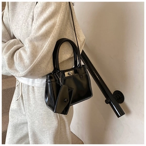 Glossy black Kelly style handbag with mini pouch accessory held by a model