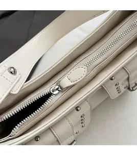 Close-up of silver zipper and rivet details on the cream motorcycle shoulder bag
