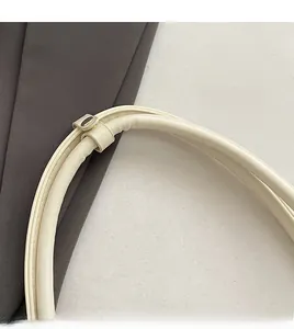 Close-up of the cream-colored underarm bag strap with polished gold metal buckle
