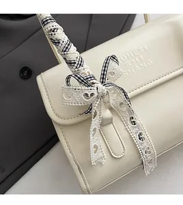 Detail of cream shoulder bag featuring lace bow decoration and embossed leather texture