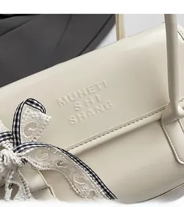 Detail of cream leather shoulder bag with embossed letters and a checkered lace bow