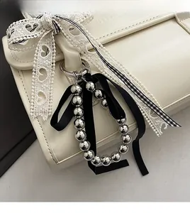 Detail of silver beaded keychain with black ribbon bow attached to a white leather bag