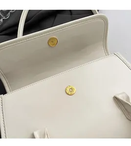 Detailed macro view of the gold magnetic closure and stitching on a beige shoulder bag