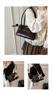 Detail of dark brown patent leather shoulder bag with lace bow and pearl chain charm