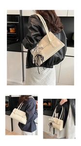 Detail of cream PU leather shoulder bag with chic bow charm and embossed logo