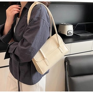 Close-up of cream rectangular shoulder bag with long handles and embossed lettering detail