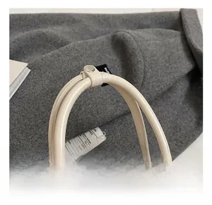 Detail of cream leather shell bag with round handle, silver rivets and dual zipper closure