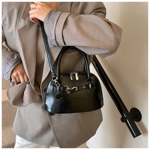 Detail of a shiny black shell bag with leather belt decoration and silver metal zipper