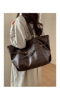 Detail of a large coffee brown tote bag featuring fine faux leather texture and gold buckles