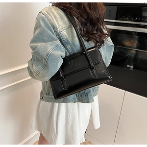 Detail of black glossy shoulder bag with embossed letters and double straps on model