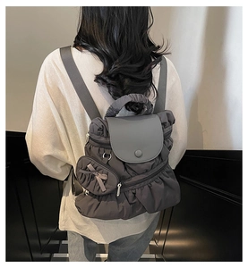 Detail of dark gray quilted backpack featuring a pleated texture and bow charm accessory