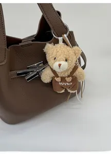 Close-up of a cute plush bear charm with corduroy overalls on a leather bucket bag