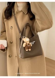 Detail of dark brown lychee leather bucket bag with cute teddy bear charm accessory